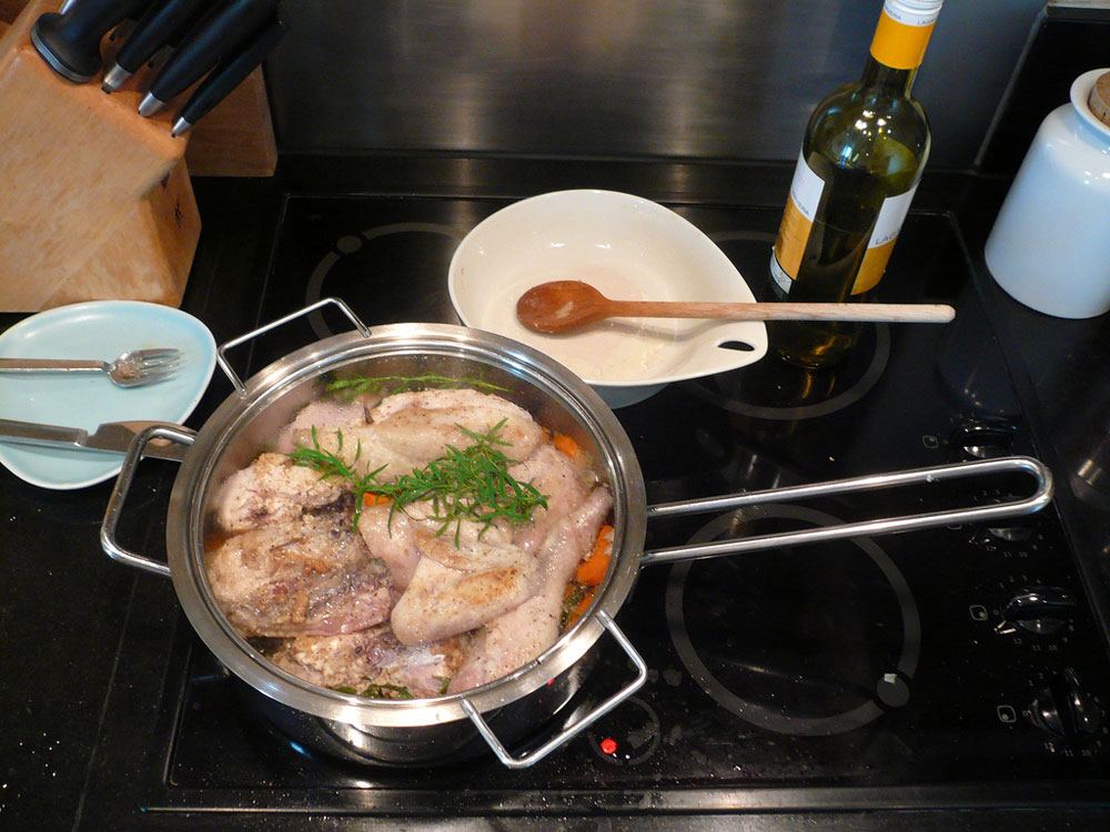 a chicken pot on the gas stove, knife, fork, spoon and a bottle of wine on the table