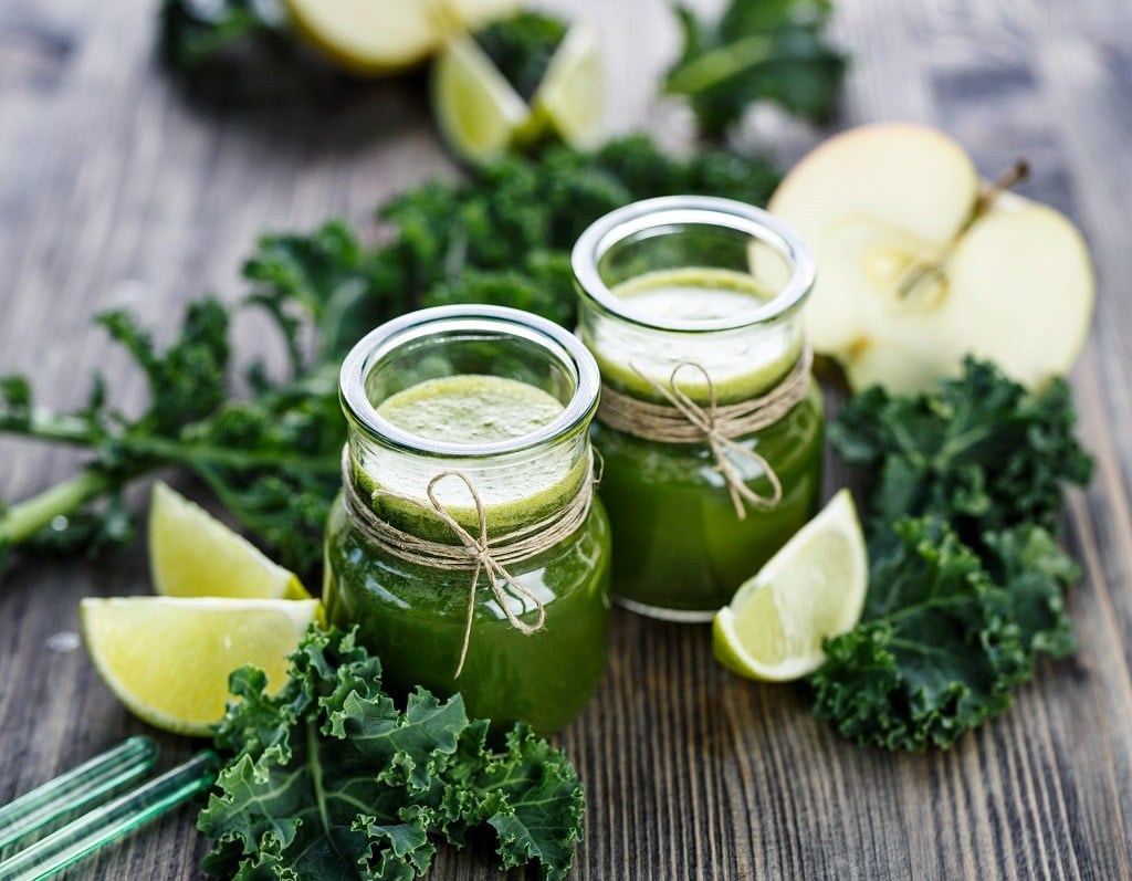 bottles of Kale Juice, slices of lemon and slices of apple