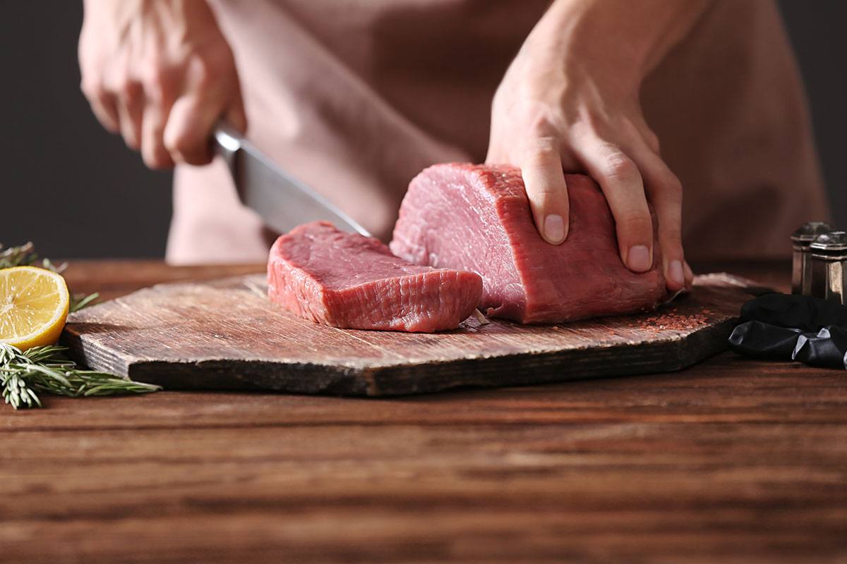 A man uses the butcher knife to cut the meat on the chopping board