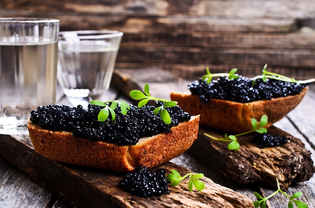 Pieces of bread with caviar and cheese and cups of water