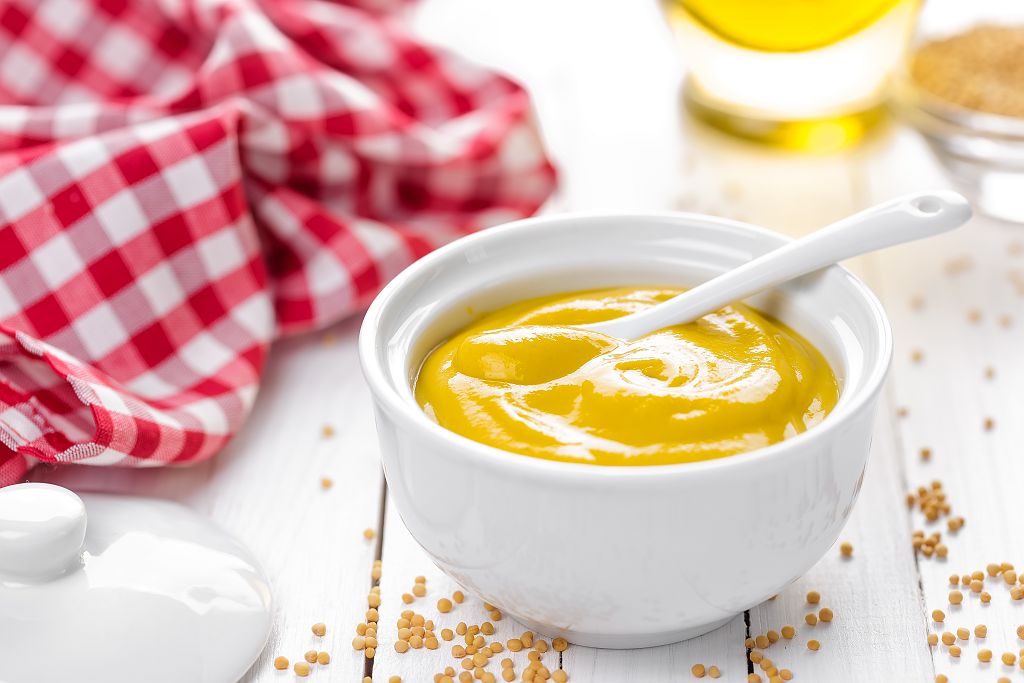 a bowl of Yellow mustard and a spoon