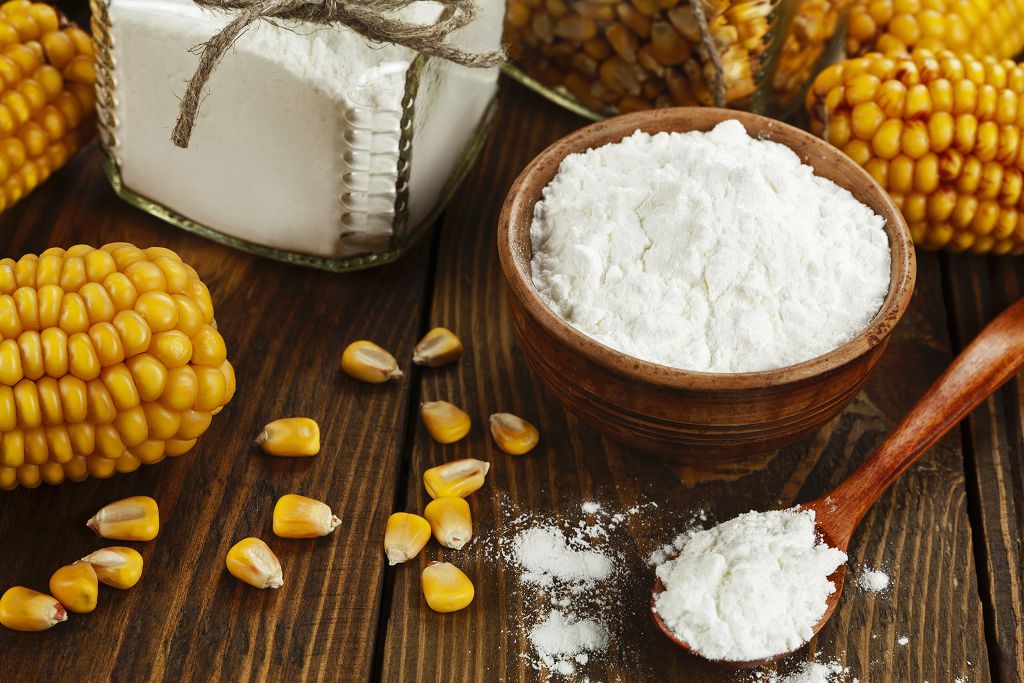 a bottle, a spoon and a bowl of Cornstarch and corn on the table